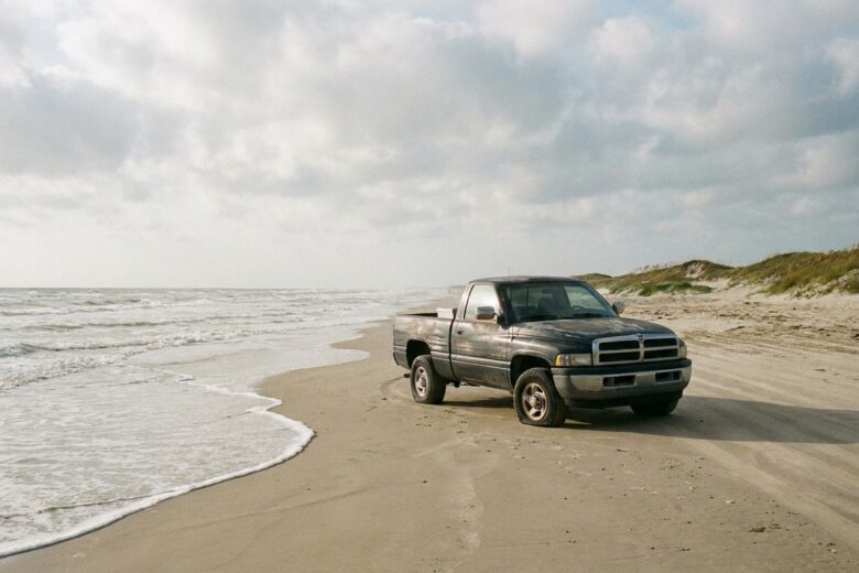 Four-wheel drive vehicle on Texas beach sand near the Gulf waterline with coastal dunes visible