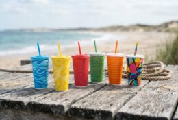 Collectible beverage cups displayed on coastal wooden surface with beach elements