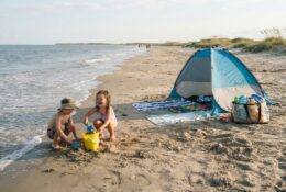 Minimalist family beach setup with shade tent and children playing in sand near Texas coastline