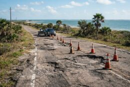 Damaged coastal road with potholes and warning cones in Corpus Christi
